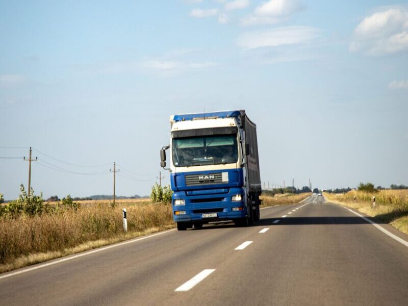 A blue truck drives along a rural road on a clear day, showcasing transportation and travel.